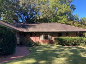 Single-story brick house with sloped tile roof surrounded by trees and lawn
