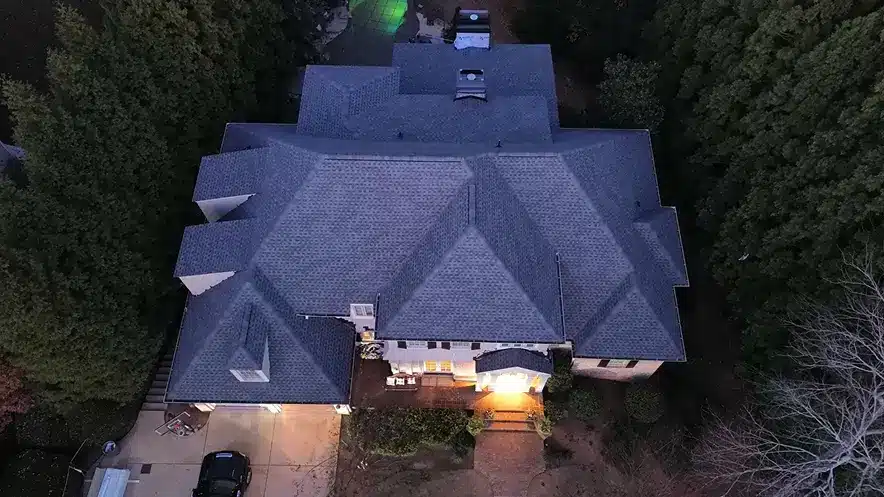 Aerial view taken at dusk displaying fully repaired residential roof surrounded by trees, showcasing roof repair process by Skyline Contracting