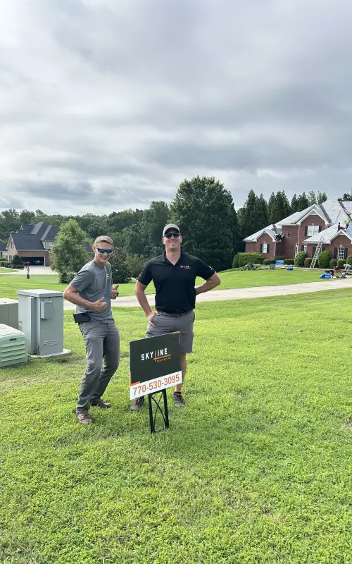 Two Skyline Contracting professionals standing beside branded sign on residential lawn, marking the start of the roof repair process