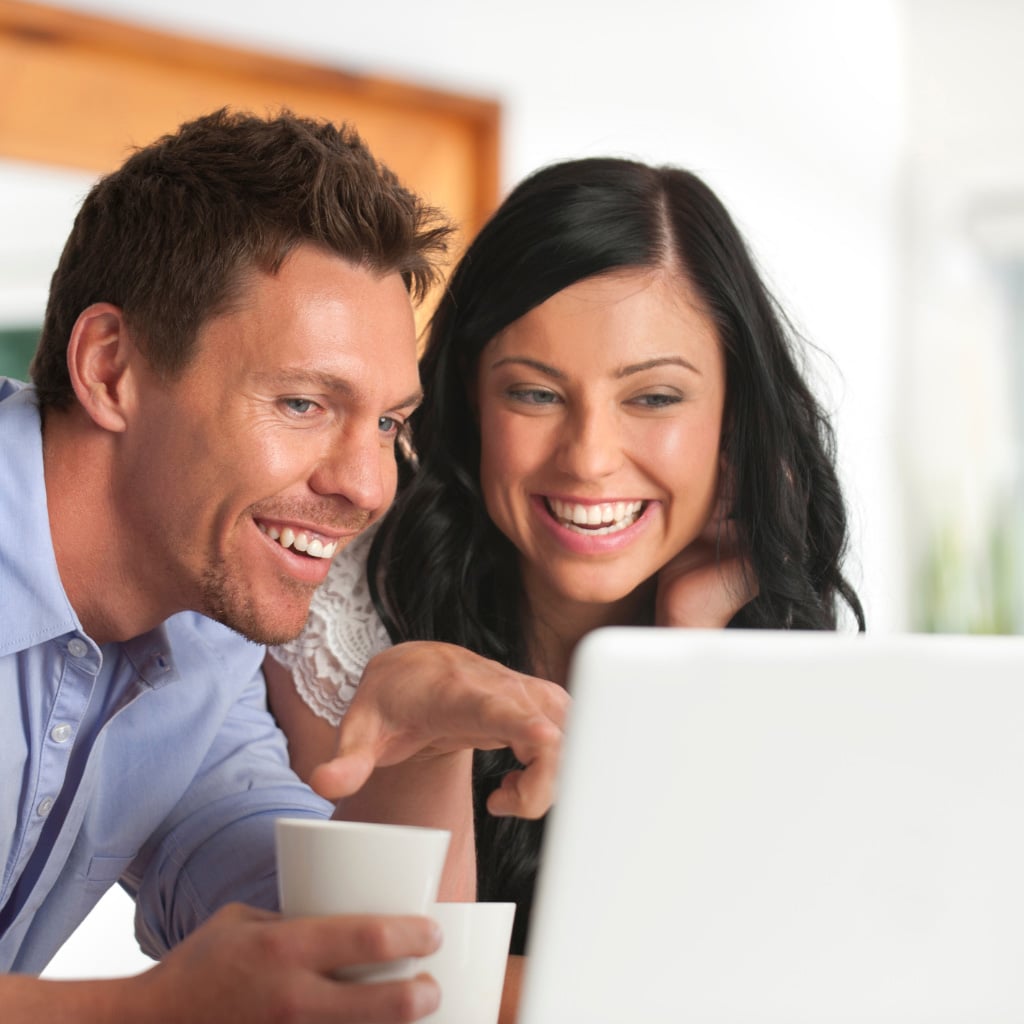 Smiling couple looking at a computer laptop together smiling over coffee