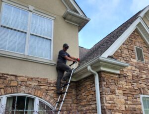 a roofer on a ladder inspects a roof for signs of a leak