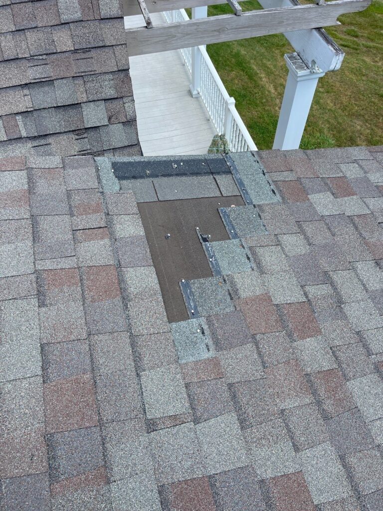 A damaged roof with missing shingles and a wooden porch railing on the side.