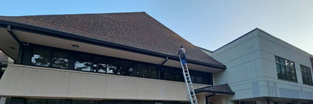 A commercial establishment with certified roofing specialists on a ladder doing roof maintenance