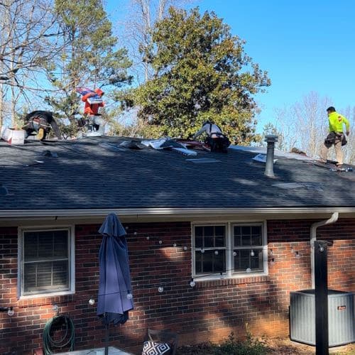 Skyline Contracting residential roofing services contractors are installing a new roof on a single-story brick house under a bright blue sky in Gainesville, GA