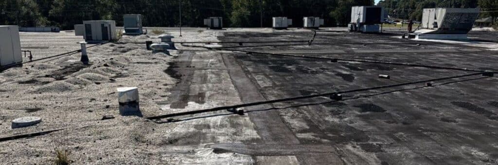 A slightly angled aerial view of a flat, commercial rooftop with various HVAC units and pipes, showing signs of wear and needing commercial roof repair by Skyline Contracting in Gainesville, GA