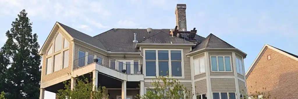 Large beige house on Lake Lanier in Gainesville, GA with steep roof under replacement by Skyline Contracting contractors