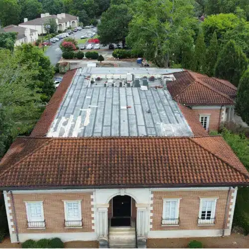 Top-down aerial of a weathered flat roof membrane bordered by red clay tile hips and ridges before maintenance in Gainesville.