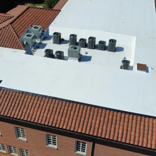 Close aerial of rooftop HVAC on white membrane beside red clay tile eave, showing curb and flashing details after maintenance in Gainesville.