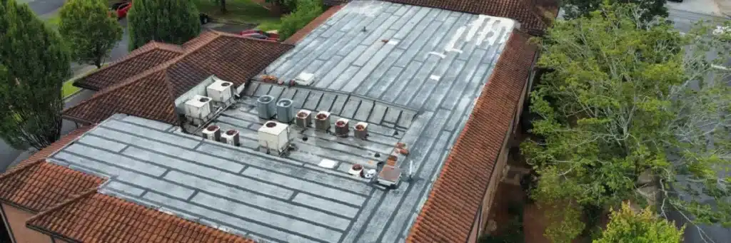 Angled aerial of weathered flat roof with equipment and surrounding red clay tiles during maintenance, showing worn seams and patches in Gainesville.