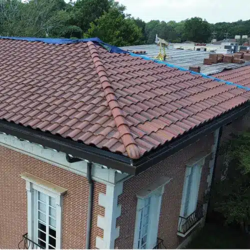 Oblique aerial of red clay tile roof with ridge caps and a blue tarp during maintenance on a brick building in Gainesville