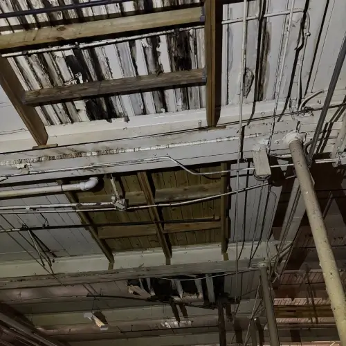 Exposed industrial ceiling with extensive rot, damaged beams, and roof leak repair cost issues visible, inspected by Skyline Contracting