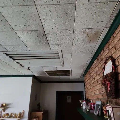 Water stains and discoloration on interior ceiling tiles above brick fireplace indicating roof leak and associated roof leak repair cost by Skyline Contracting