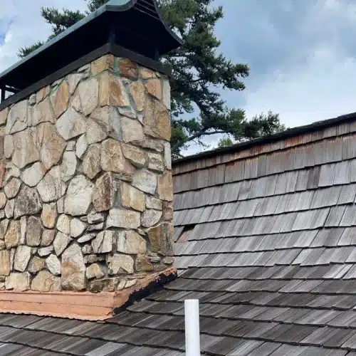 Stone chimney with counterflashing and step flashing on a wood shake roof, a frequent roof inspection problem area, by Skyline Contracting in Gainesville