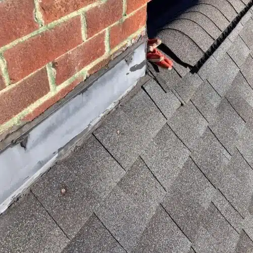 Asphalt shingles meeting a brick chimney with step flashing and sealant, checked for gaps and water intrusion—roof inspection problem areas by Skyline Contracting in Gainesville