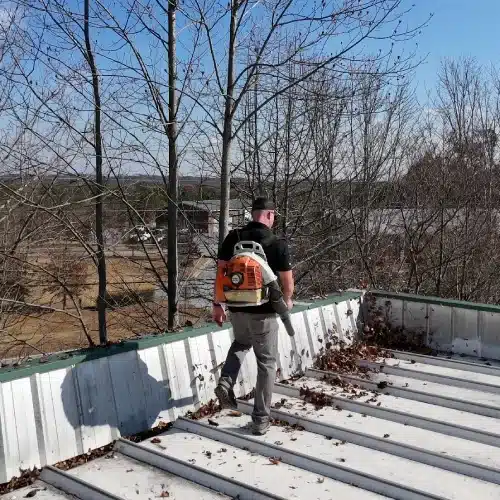Technician clearing leaves from a standing seam metal roof near the gutter to prevent clogs and leaks—roof inspection problem areas—by Skyline Contracting in Gainesville