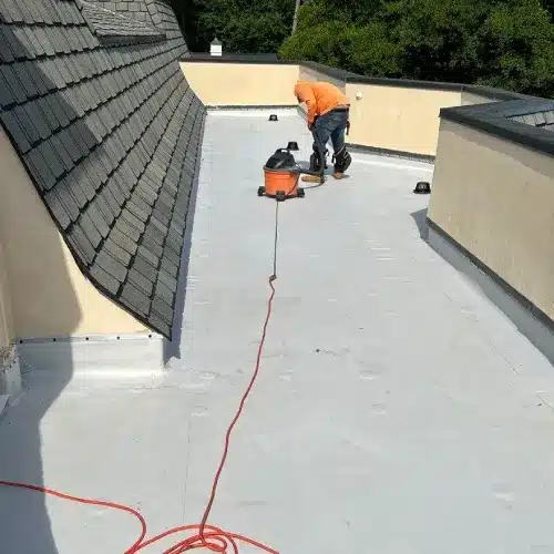 Roofing technician using a vacuum to clean a flat roof surface for easier maintenance by Skyline Contracting | Roofing Contractor & Remodeler in GA