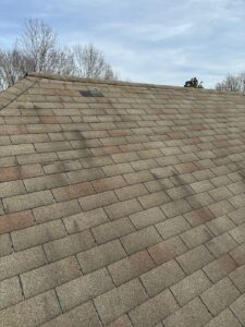 A close-up of an asphalt shingle roof with visible wear and patchwork repairs, showing roofing concerns related to warranty coverage.