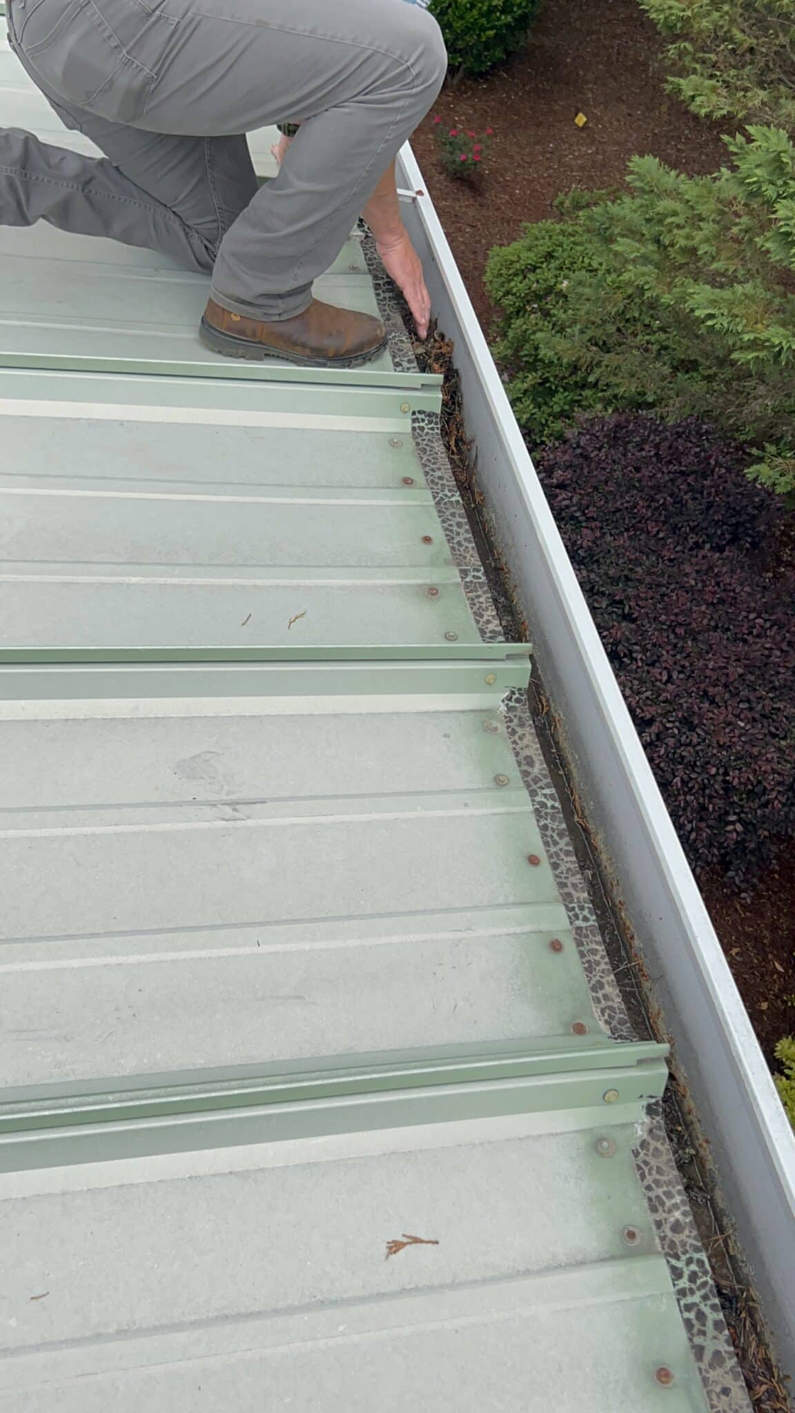 A roofer inspecting standing seam metal roofing near the gutter line, supporting spring roof maintenance in Gainesville by Skyline Contracting.