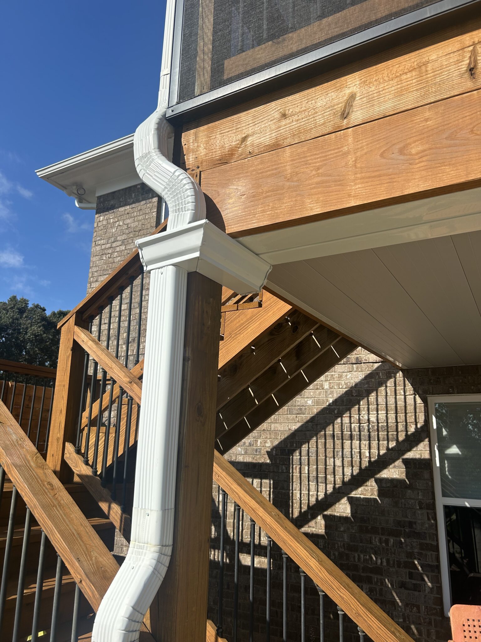 A new white decorative residential downspout section meticulously installed on a custom wooden deck frame to resolve visible new gutters signs gutter installation service in Gainesville by Skyline Contracting