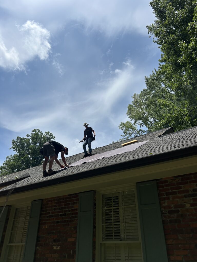 Two roofing professionals working on a residential asphalt shingle roof under a bright blue sky to complete a comprehensive roofing maintenance checklist roofing service in Gainesville by Skyline Contracting