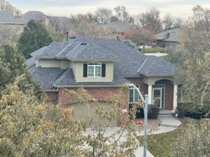 Aerial view of a multi-gabled suburban home with dark architectural shingles surrounded by autumn trees demonstrating fall roofing tips residential roof maintenance in Omaha by Anchor Roofing