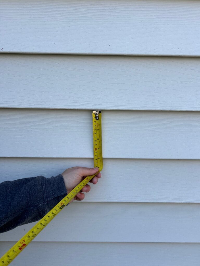 A contractor holding a yellow tape measure against light blue lap siding panels during a house siding replacement process siding replacement service in Gainesville by Skyline Contracting