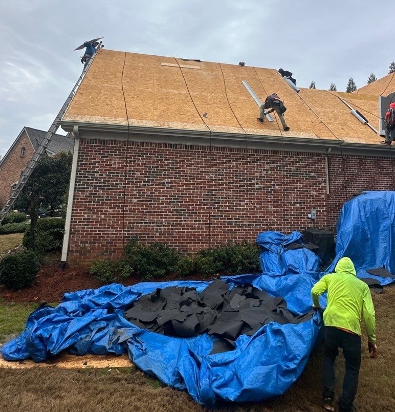A roofing crew stripping old shingles onto blue protective tarps during an insurance roof replacement roofing service in Gainesville by Skyline Contracting