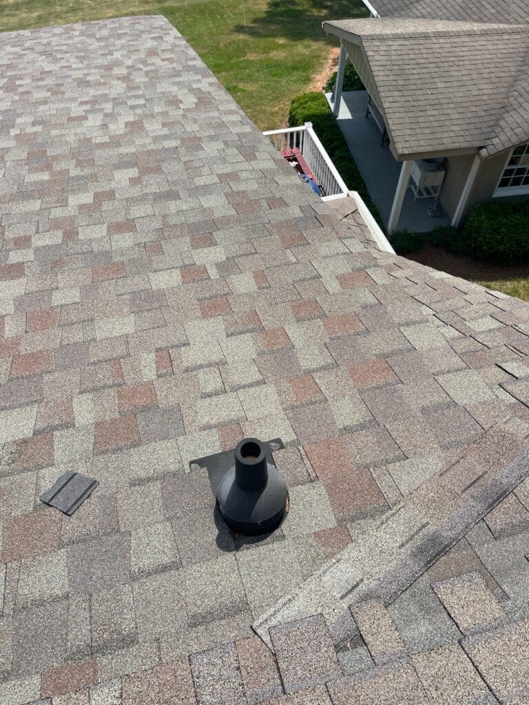 An elevated view looking down a pitched multi-tone asphalt shingle roof featuring a black pipe boot flashing and minor shingle debris to satisfy roof damage insurance claim rules roofing service in Gainesville by Skyline Contracting